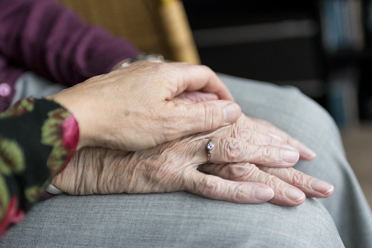 An older woman's hand resting on her mother's hand, in her lap