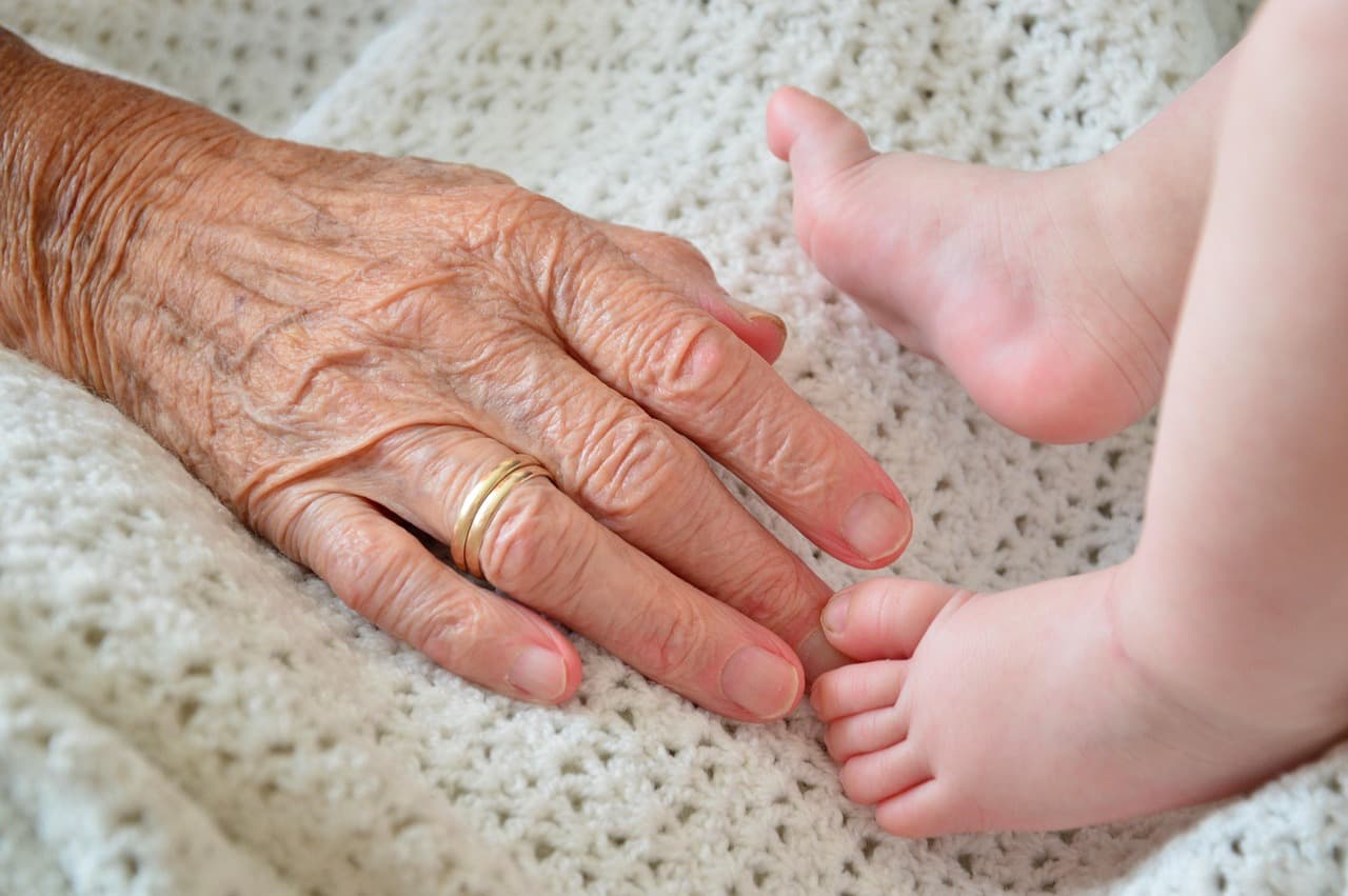 A grandparent's hand beside a baby's foot on a knitted blanket