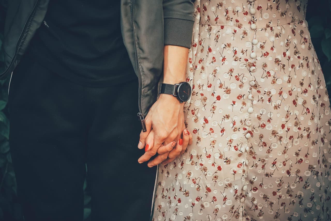 A couple holding hands, her floral dress beside his dark jacket
